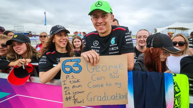 A Mercedes fan holds a sign asking George Russell to go to his graduation