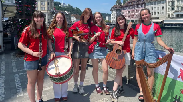 Six young Welsh musicians with their traditional instruments, smiling at Lucerne's waterfront