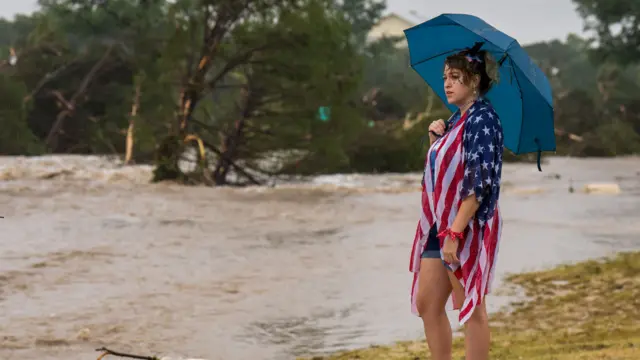 A woman draped in an American flag holds an umbrella after flooding in Kerrville, central Texas