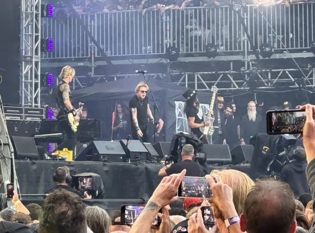 A group on stage and the backs of people's heads in the crowd