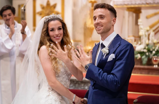 Rute Cardoso and Diogo Jota smiling at the alter at their wedding, with Ruth Cardoso showing the ring on her hand to the camera