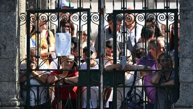 Public mourners gather at the funeral outside metal railings