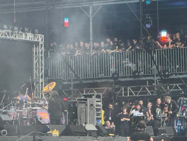 People watching standing by railings near the stage.