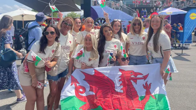 A group of women in custom Cymru Lily Woodham tops, smiling and holding Welsh flags