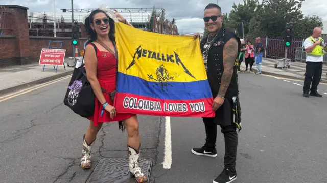 A man and woman stand holding a Columbian flag, which is decorated with the words "Metallica, Columbia loves you".
