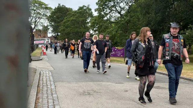 People are walking down a path, dressed in variations of black. They are wearing metal band or Black Sabbat t-shirts
