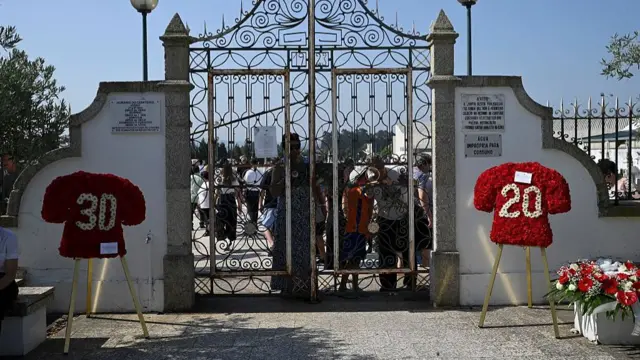 Red wreaths in the shape of football jerseys, one with the number 20 and the other with the number 30, are displayed at the entrance of a cemetery