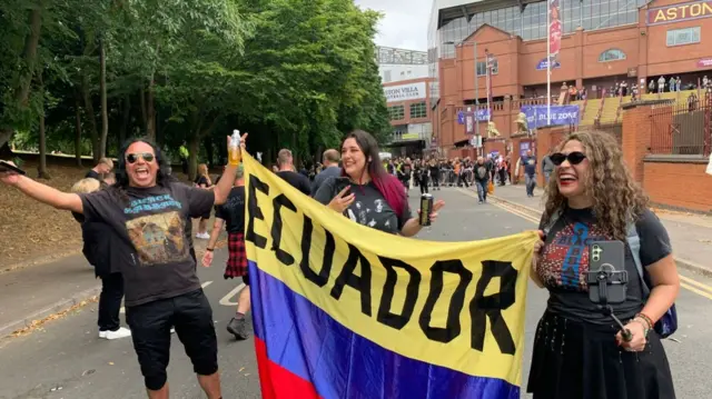 Two people smiling holding a flag outside Villa Park