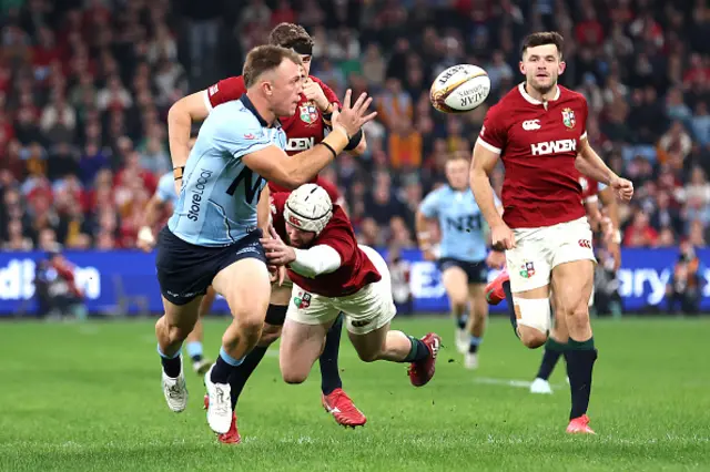Darby Lancaster of the Waratahs offloads as he is tackled by Mack Hansen