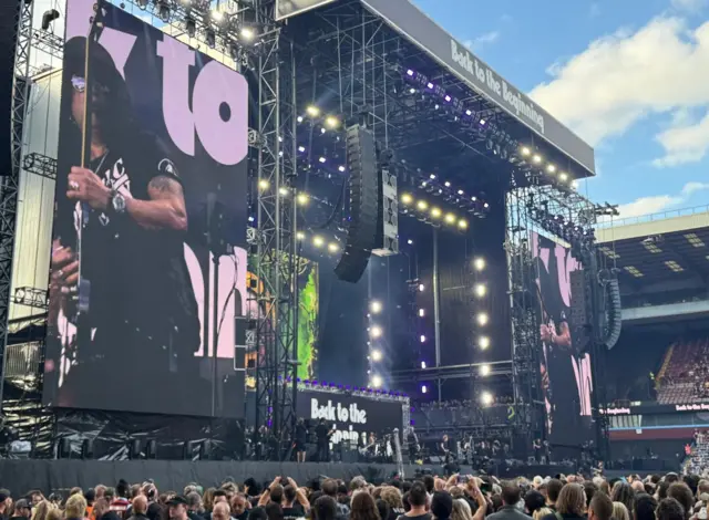 Someone performing is visible on the big screen on the left and the crowd are on the ground.