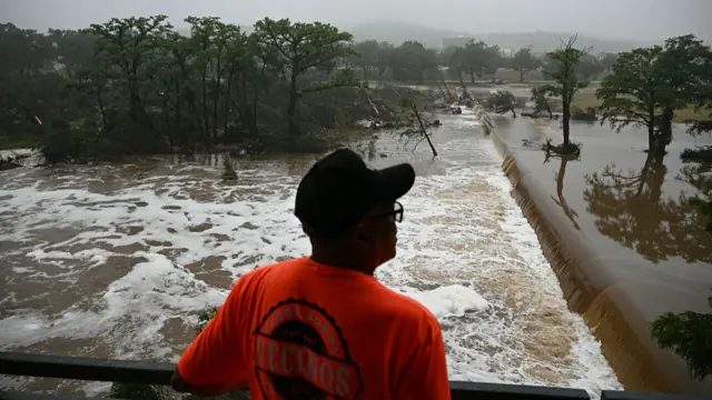 A man in a red shirt and cap looks out at flooding caused by a flash flood at the Guadalupe River in Kerrville, Texas, on July 5, 2025