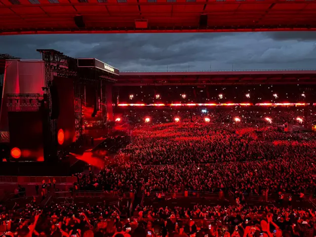 Red light bathes a concert crowd of thousands in front of a stage