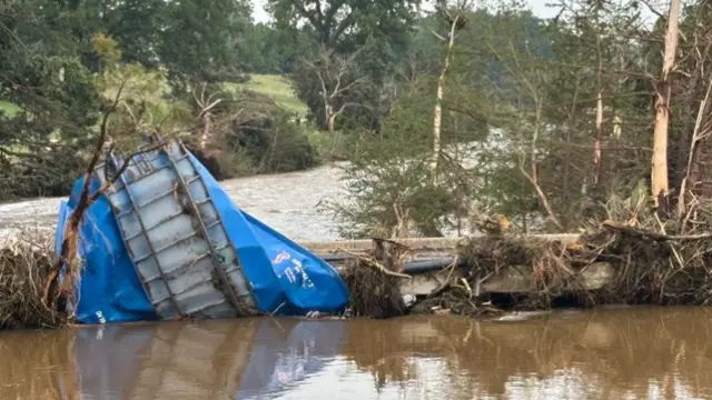 A several-ton blue dumpster fully flattened against a walkway, half-submerged under water.