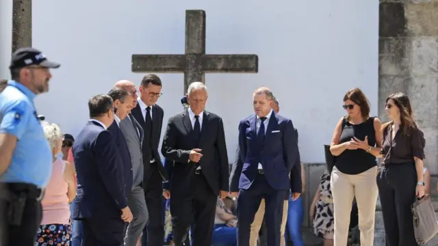 Portugal's President, Marcelo Rebelo de Sousa, centre, in Gondomar on Friday. Alt text: Portugal’s president, surrounded by a small group, walks with a cross in the background