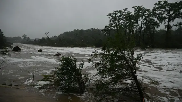 Flooding caused by a flash flood at the Guadalupe River in Kerrville, Trees partially submerged and bent as the water rushes by