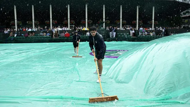 Ground staff sweep rain off the rain covers