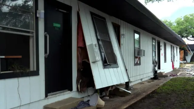 Wide shot of external wall of white wooden bungalow with one panel partially raised as a result of flooding