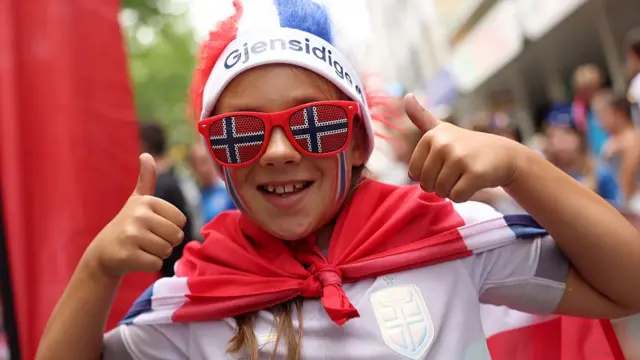 A fan of Norway poses for a photo while wearing fancy dress and sunglasses in the colours of the teams national flag, as they enjoy the pre-match atmosphere prior to the UEFA Women's EURO 2025 Group A match between Norway and Finland at Stade de Tourbillon
