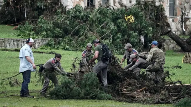 Several emergency personnel trying to move vegetation strewn on the ground at Camp Mystic in Kerr County