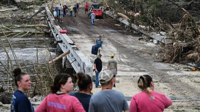 People look on as law enforcement and volunteers continue to search for missing people near Camp Mystic,