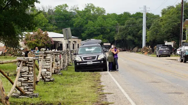Two women hug on the side of the road next to a black pick-up trick