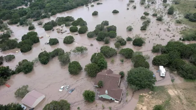 Houses and cars partially submerged in muddy flood waters near Kerrville, Texas