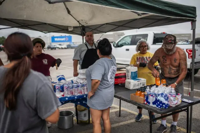 People under a pop-up tent with bottles of water and meals in takeaway containers.