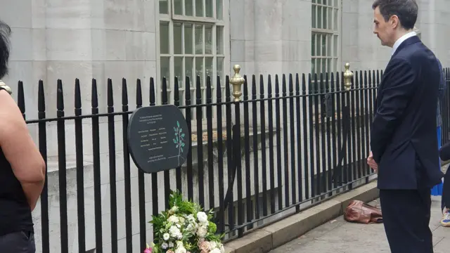 BMA staff member stands in front of wreath and memorial
