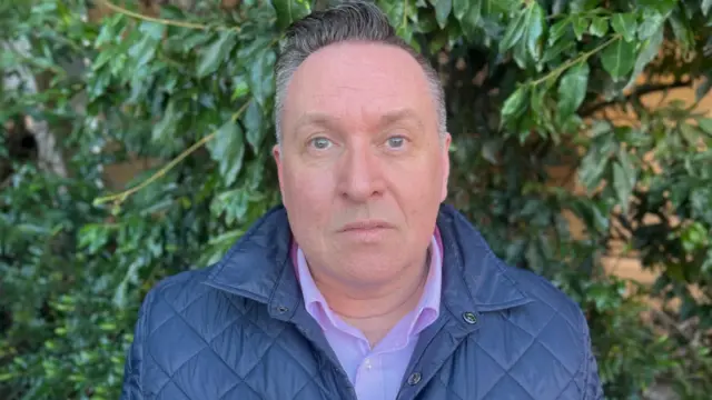David Peters, one of the attendees in court, looking at camera, wearing blue jacket with background of greenery