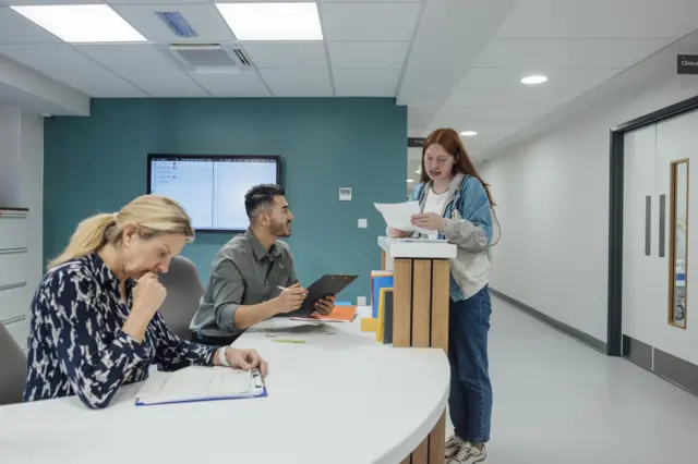 Side view wide shot of a medical professional helping a patient sign in while working at a hospital