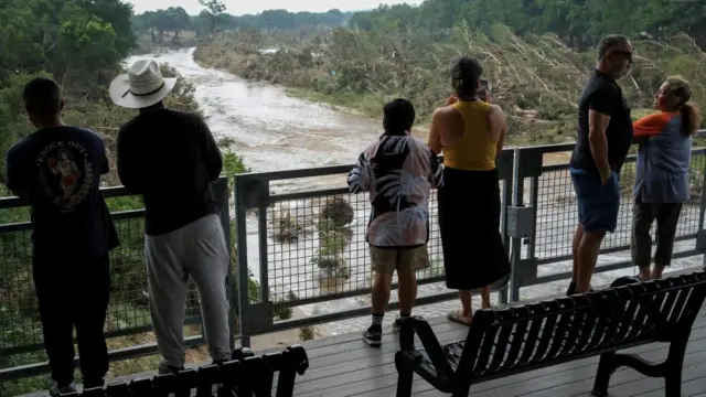 A group of people stand on a viewing platform looking over the river