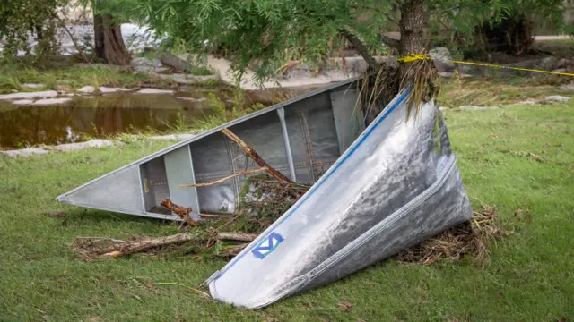 A silver canoe is bent almost in half around the trunk of a small tree