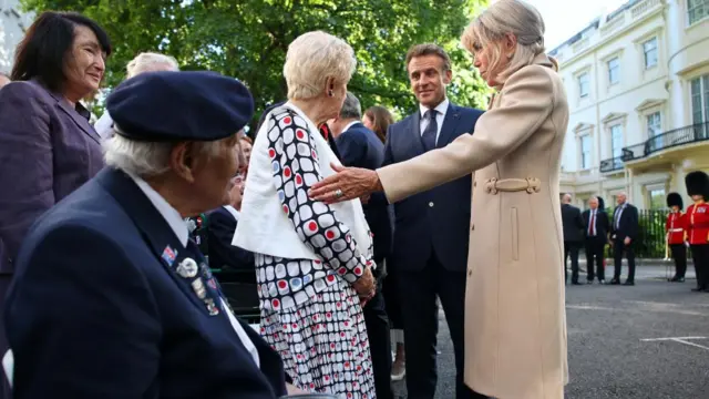 Emmanuel and Brigitte Macron speak to a woman wearing a white patterned dress