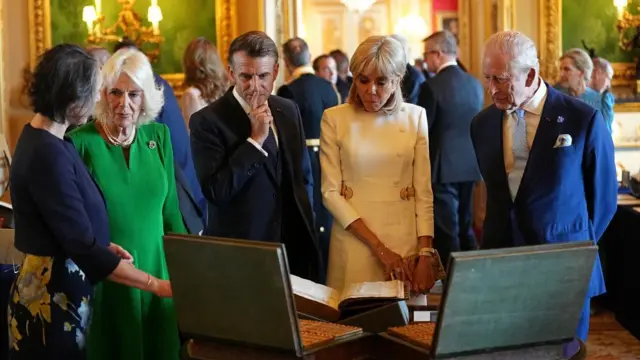 King Charles III and Queen Camilla with the President of France Emmanuel Macron and his wife Brigitte Macron view items on display during a visit to the Royal Collection exhibition, in the Green Drawing Room at Windsor Castle.