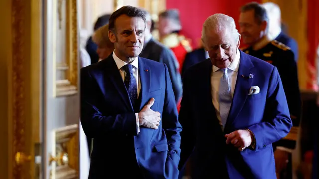 Macron and Charles wear suits and walk ahead.