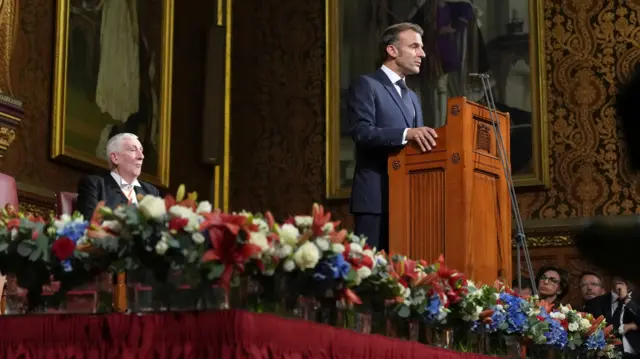 Macron stands at a lectern, delivering a speech.