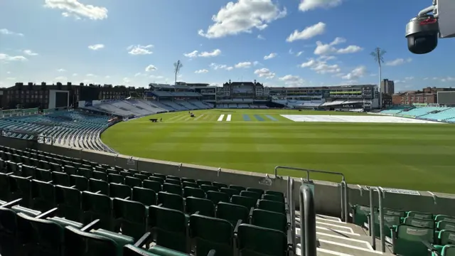 An empty Oval stadium with green grass on the cricket pavilion and clouds dotted around above on a blue sky