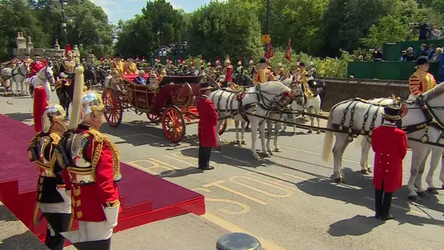 A carriage with four horses pulling it and multiple people stood around