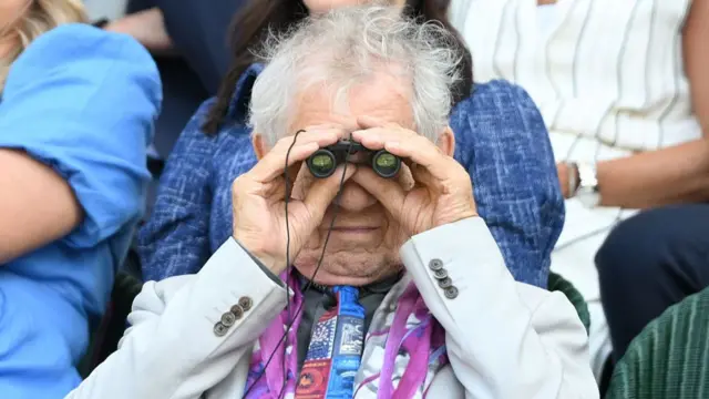 Sir Ian McKellen looks through binoculars from royal box on Centre Court
