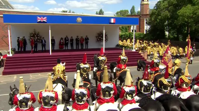 Rows of mounted cavalry and a band in front of a stage with some people on it