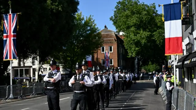Dozens of police officers stand in a line on a street in Windsor with barriers. A French and British flag have been raised.