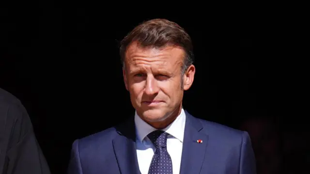 Macron looks ahead wearing a suit.
