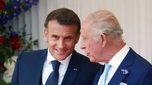 French President Emmanuel Macron (L) and Britain's King Charles III speak. Macron smiles.