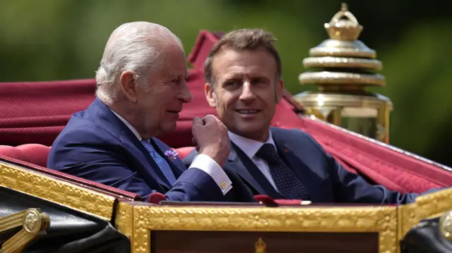 Macron and Charles speak while sitting in a carriage.