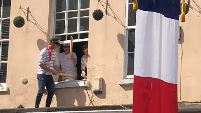 Men wearing striped tops and holding baguettes can be seen in a window with a French flag in the foreground