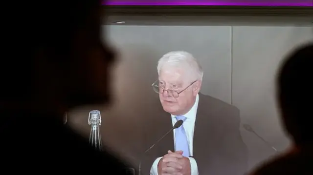 Chair of the Post Office Horizon IT Inquiry, Sir Wyn Williams, is seen on a live feed as he makes a statement as the first volume of a report from the Post Office Horizon IT Inquiry