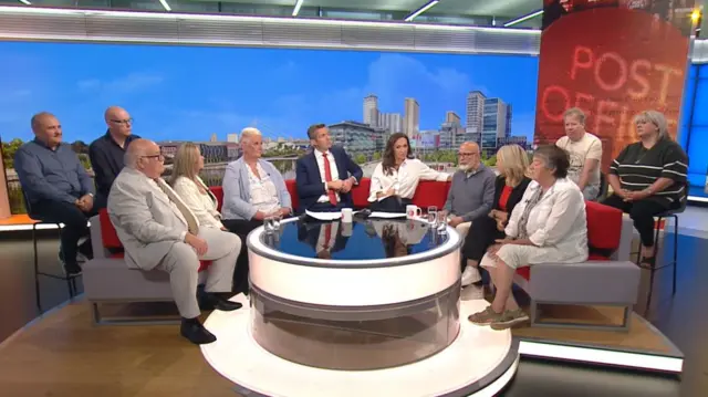 Wide shot of BBC Breakfast studio with presenters (C) surrounded by four former Post Office submasters and six former Post Office submistresses