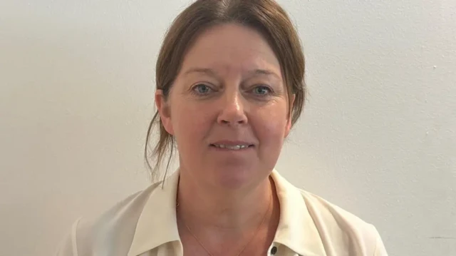 Kathy McAlerney has brown hair tied back and is wearing a white shirt.