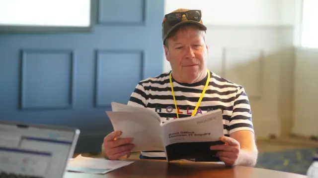 Scott Darlington, in a black and white stripy t-shirt, reads a report at a desk