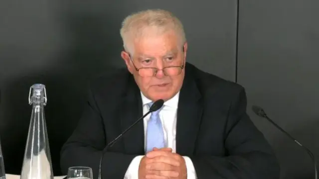 Wyn Williams speaking into a microphone at the inquiry. He has short grey hair and is wearing wire black framed glasses.